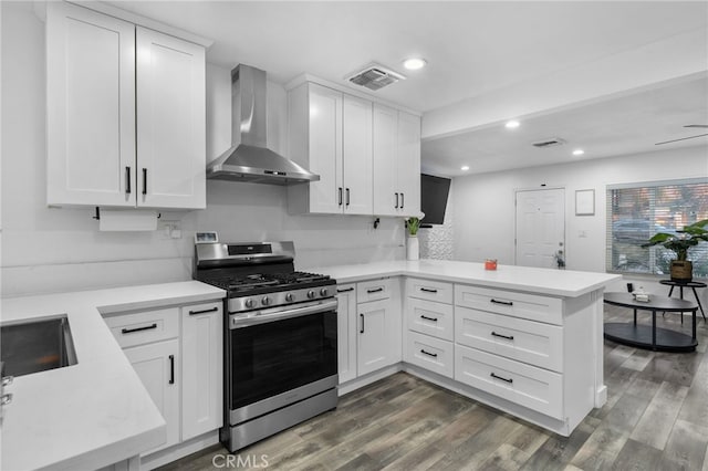 kitchen featuring white cabinetry, kitchen peninsula, stainless steel range with gas stovetop, dark wood-type flooring, and wall chimney range hood