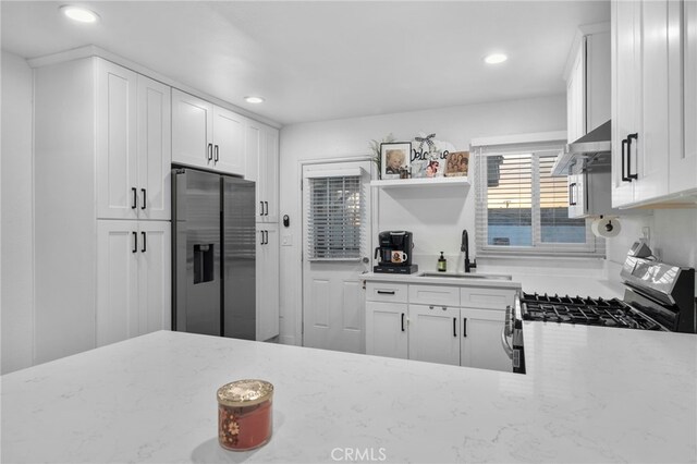 kitchen with stainless steel fridge with ice dispenser, gas stove, white cabinets, light stone counters, and sink