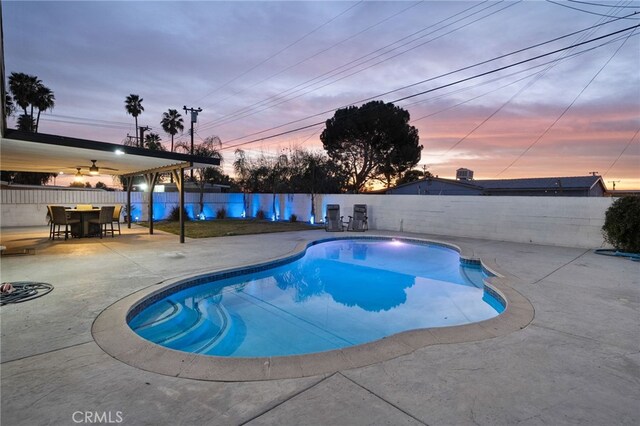 pool at dusk featuring ceiling fan and a patio