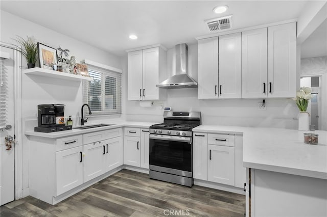 kitchen featuring white cabinets, wall chimney range hood, stainless steel gas stove, sink, and dark hardwood / wood-style floors