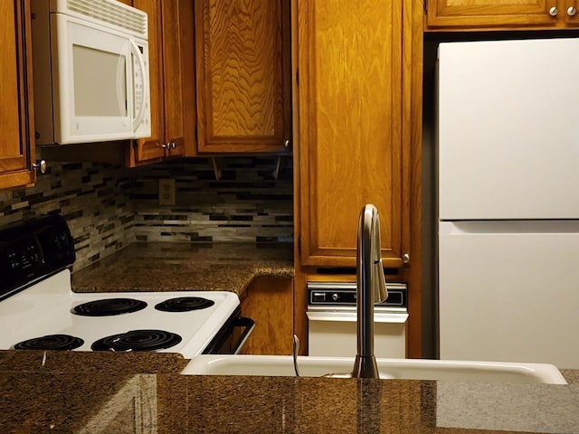 kitchen featuring decorative backsplash, white appliances, and dark stone counters