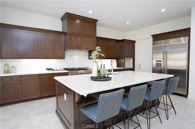 kitchen with a kitchen bar, appliances with stainless steel finishes, an island with sink, and dark brown cabinetry