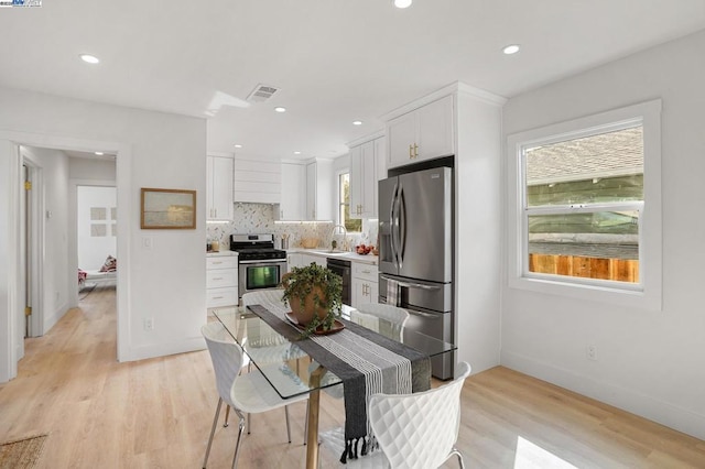 kitchen featuring appliances with stainless steel finishes, backsplash, light wood-type flooring, white cabinets, and sink