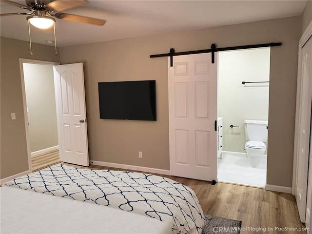 unfurnished bedroom featuring connected bathroom, light hardwood / wood-style floors, a barn door, and ceiling fan