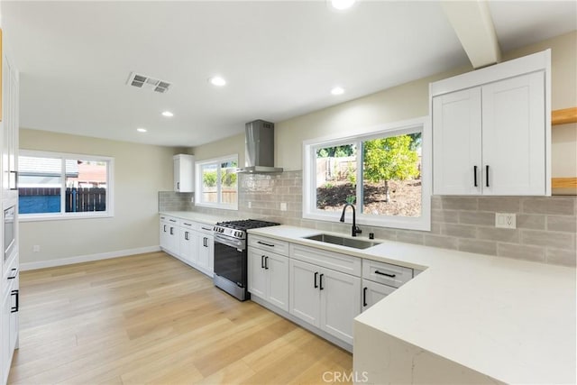 kitchen with white cabinets, wall chimney exhaust hood, decorative backsplash, sink, and stainless steel gas range oven