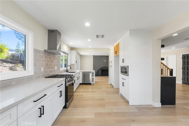 kitchen with tasteful backsplash, wall chimney range hood, sink, white cabinetry, and appliances with stainless steel finishes