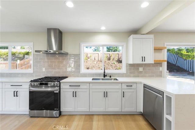 kitchen featuring wall chimney range hood, appliances with stainless steel finishes, sink, and white cabinetry