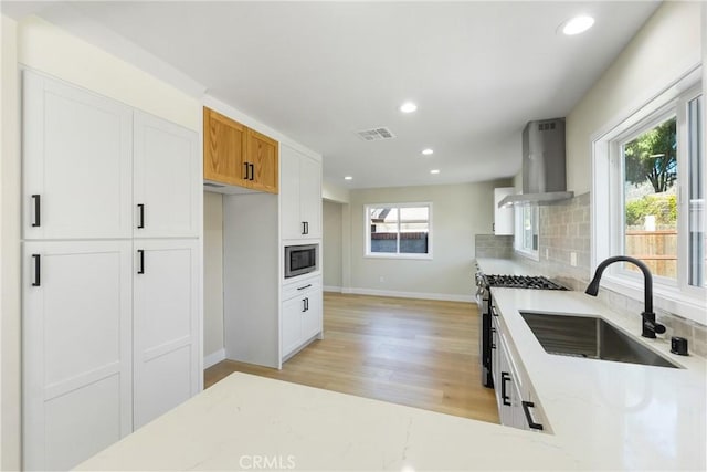 kitchen featuring sink, white cabinets, built in microwave, and wall chimney range hood