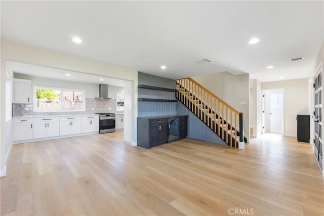 kitchen featuring white cabinets, stainless steel range, wall chimney range hood, and light hardwood / wood-style flooring