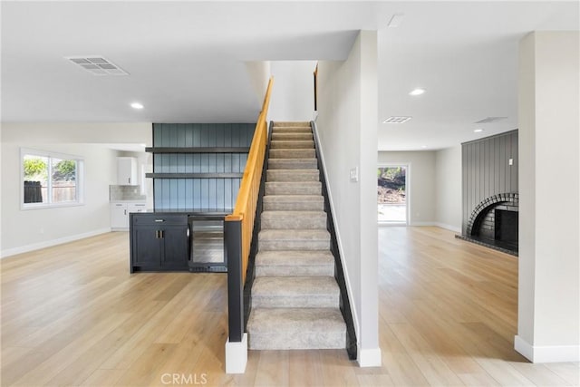 stairway featuring wine cooler, a fireplace, a wealth of natural light, and hardwood / wood-style flooring