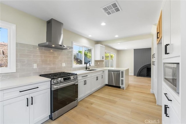 kitchen with tasteful backsplash, wall chimney range hood, sink, white cabinetry, and appliances with stainless steel finishes