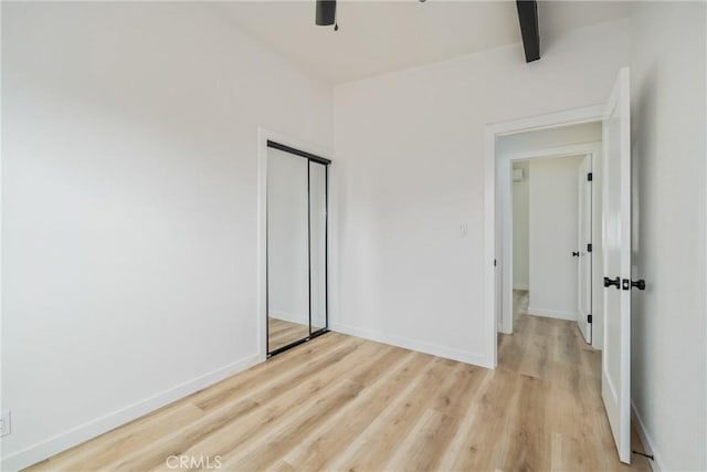 unfurnished bedroom with a closet, beamed ceiling, and light hardwood / wood-style floors