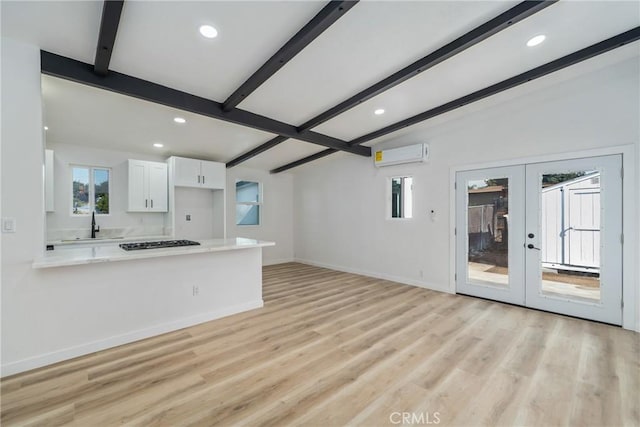 unfurnished living room with an AC wall unit, vaulted ceiling with beams, sink, light hardwood / wood-style flooring, and french doors