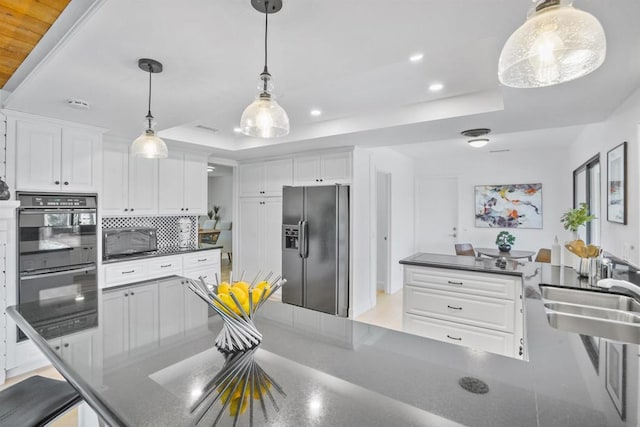 kitchen with a raised ceiling, stainless steel fridge with ice dispenser, sink, white cabinetry, and black double oven