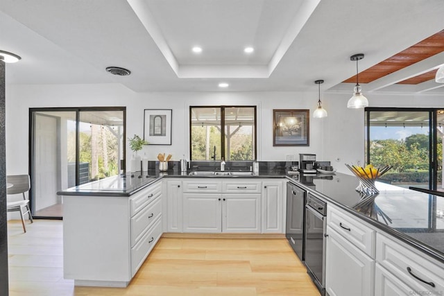 kitchen with hanging light fixtures, kitchen peninsula, a tray ceiling, white cabinets, and sink