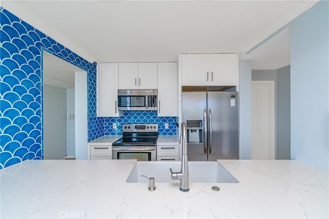 kitchen with backsplash, appliances with stainless steel finishes, light stone counters, and a sink