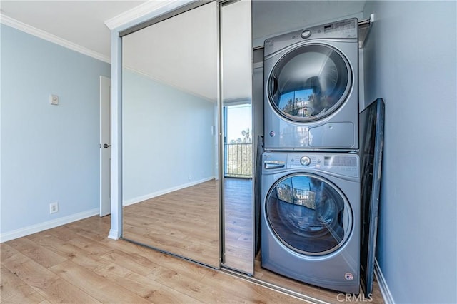 washroom featuring laundry area, baseboards, ornamental molding, stacked washing maching and dryer, and light wood finished floors