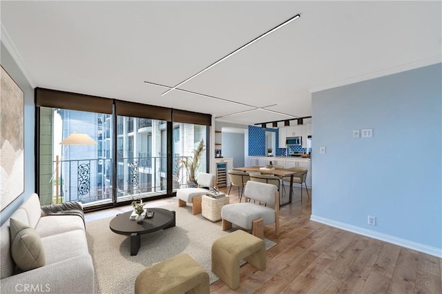 living room featuring wine cooler, baseboards, ornamental molding, light wood finished floors, and a wall of windows