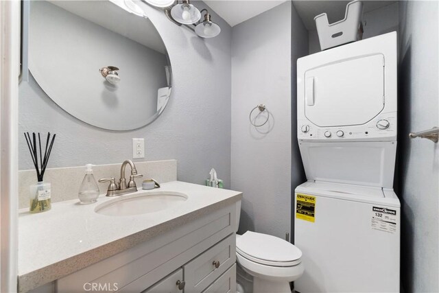 bathroom with toilet, vanity, and stacked washer and clothes dryer