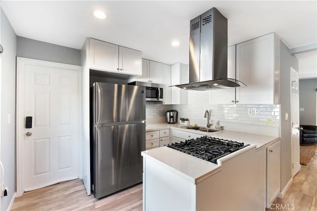 kitchen featuring white cabinetry, stainless steel appliances, light wood-type flooring, wall chimney range hood, and sink