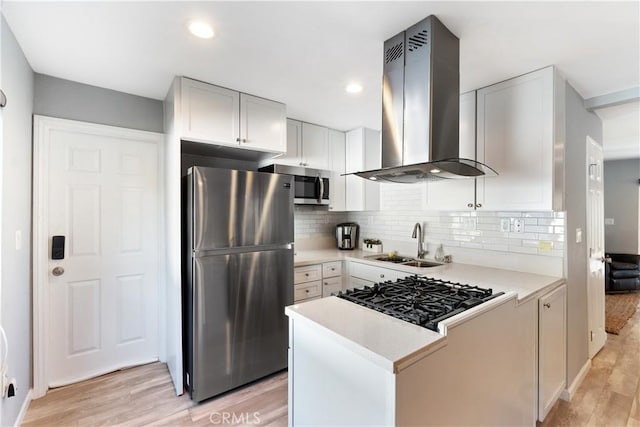 kitchen featuring island range hood, a sink, white cabinetry, light countertops, and appliances with stainless steel finishes