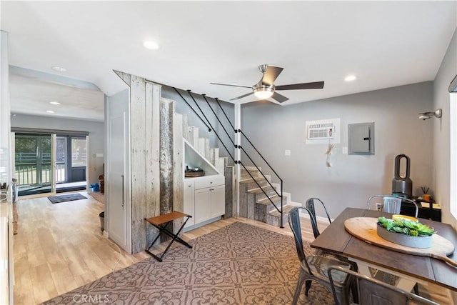 dining space featuring ceiling fan, electric panel, an AC wall unit, and light wood-type flooring