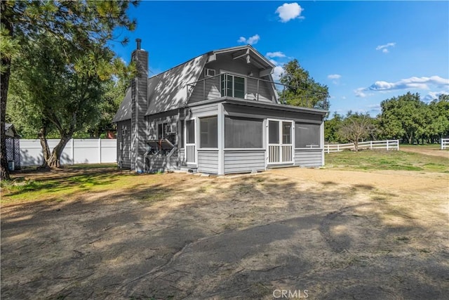 back of house with a sunroom, fence, a chimney, and a gambrel roof