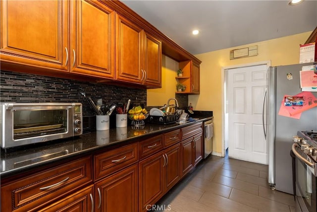 kitchen with tasteful backsplash, appliances with stainless steel finishes, dark stone counters, and dark tile patterned flooring