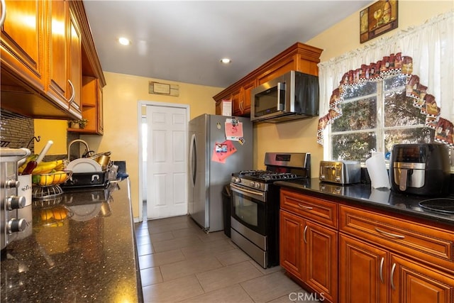 kitchen with light tile patterned floors, appliances with stainless steel finishes, and dark stone counters