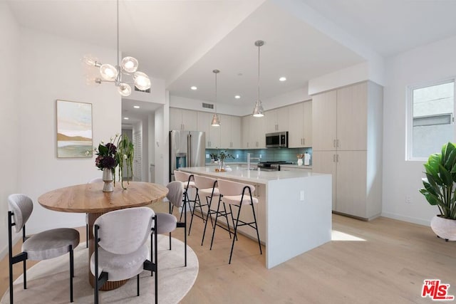 kitchen with pendant lighting, backsplash, light hardwood / wood-style floors, stainless steel appliances, and a center island with sink