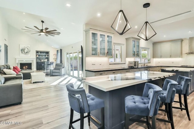 kitchen featuring lofted ceiling, wall chimney range hood, a kitchen island, hanging light fixtures, and gray cabinetry