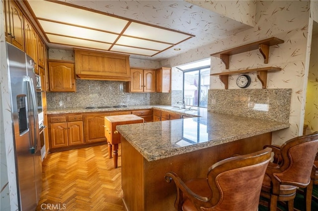 kitchen featuring stainless steel refrigerator with ice dispenser, cooktop, kitchen peninsula, light parquet floors, and a breakfast bar area