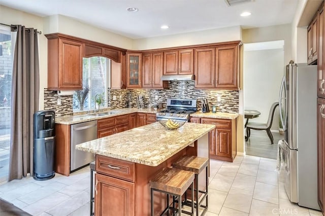 kitchen with sink, backsplash, stainless steel appliances, light stone countertops, and a kitchen island