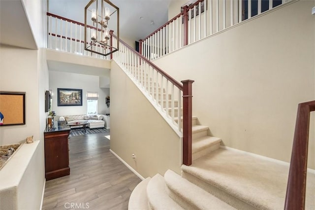 stairway with a towering ceiling, a chandelier, and hardwood / wood-style floors