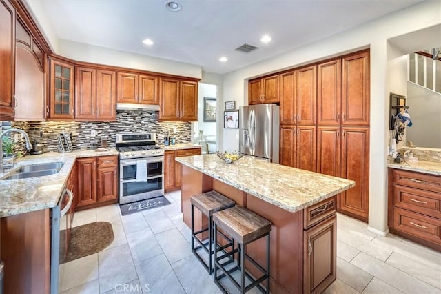 kitchen with a breakfast bar, sink, light stone counters, a center island, and appliances with stainless steel finishes