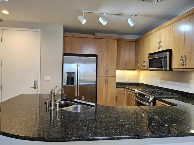 kitchen with dark stone countertops, kitchen peninsula, sink, appliances with stainless steel finishes, and rail lighting