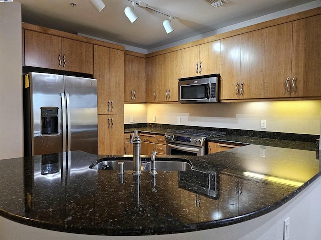 kitchen featuring rail lighting, kitchen peninsula, stainless steel appliances, dark stone counters, and sink