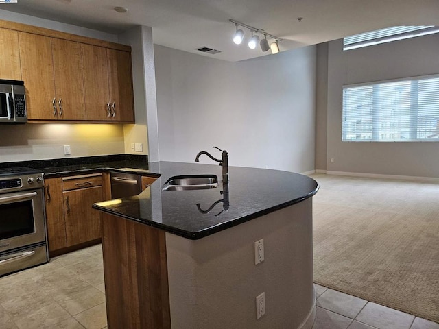 kitchen featuring light tile patterned floors, a center island with sink, stainless steel appliances, dark stone counters, and sink