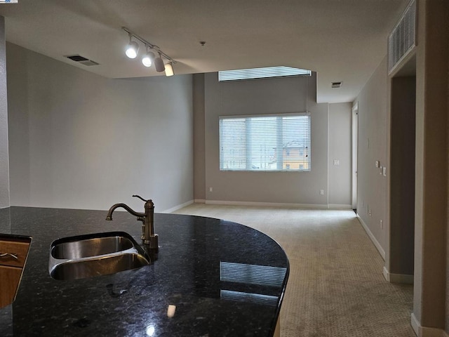 kitchen featuring sink, rail lighting, light carpet, and dark stone countertops