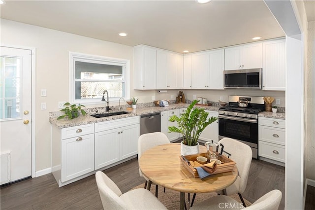 kitchen with light stone countertops, white cabinets, dark wood-type flooring, stainless steel appliances, and sink