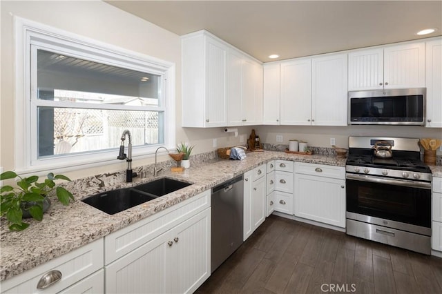 kitchen featuring dark hardwood / wood-style floors, sink, white cabinetry, appliances with stainless steel finishes, and light stone counters