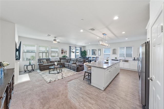 kitchen with a kitchen bar, white cabinets, a kitchen island, hanging light fixtures, and stainless steel refrigerator