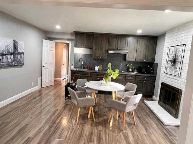 kitchen featuring a fireplace, wood-type flooring, dark brown cabinets, and tasteful backsplash