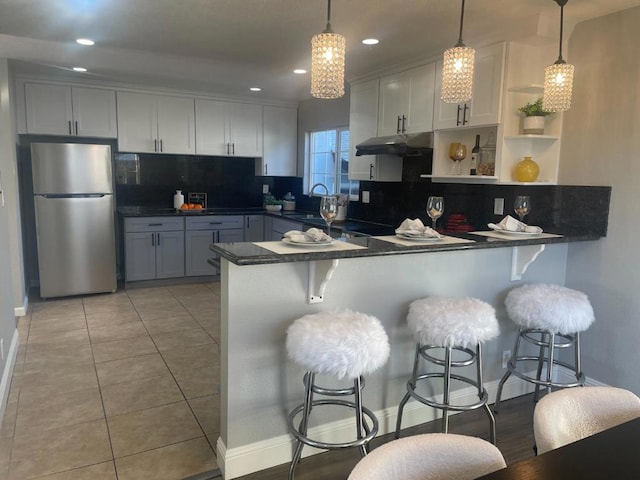 kitchen with hanging light fixtures, kitchen peninsula, stainless steel fridge, and a breakfast bar area