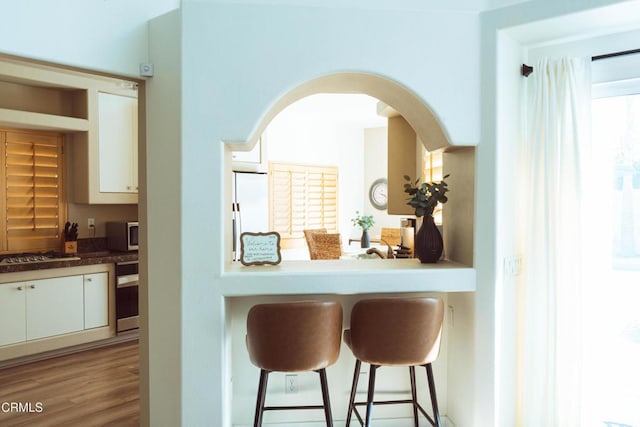 kitchen featuring a breakfast bar, stainless steel gas stovetop, white cabinets, white refrigerator, and light hardwood / wood-style flooring