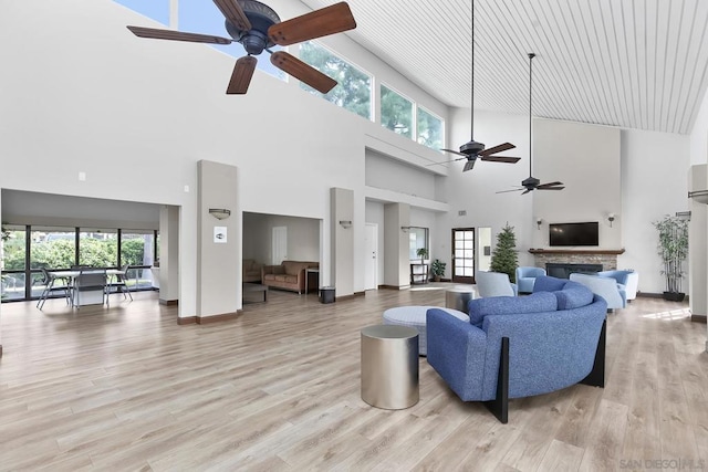 living room featuring ceiling fan, a stone fireplace, light hardwood / wood-style floors, and a high ceiling