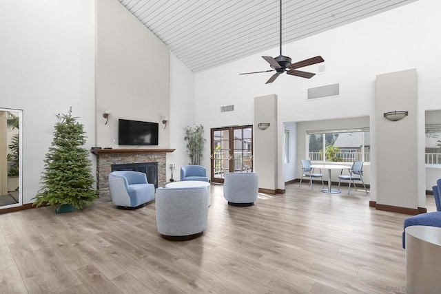 living room with ceiling fan, a towering ceiling, a stone fireplace, and wood-type flooring