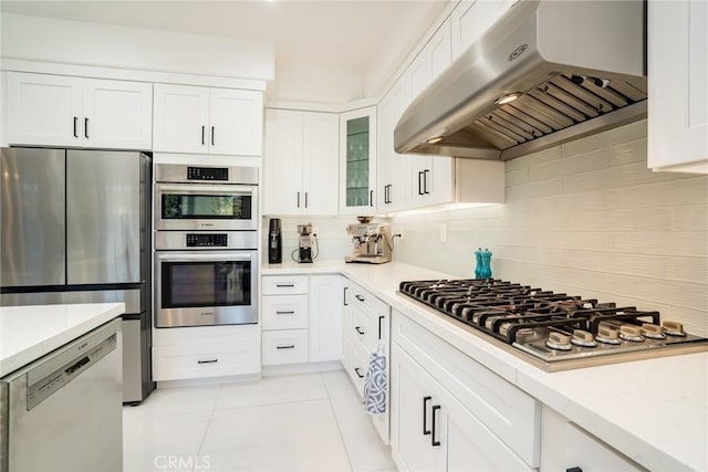 kitchen with stainless steel appliances, ventilation hood, light tile patterned floors, white cabinets, and backsplash