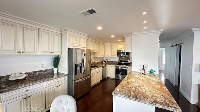 kitchen with kitchen peninsula, dark hardwood / wood-style flooring, stainless steel appliances, a barn door, and stone countertops