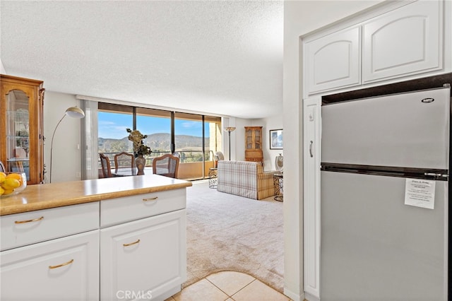 kitchen with light colored carpet, floor to ceiling windows, stainless steel refrigerator, a mountain view, and white cabinets